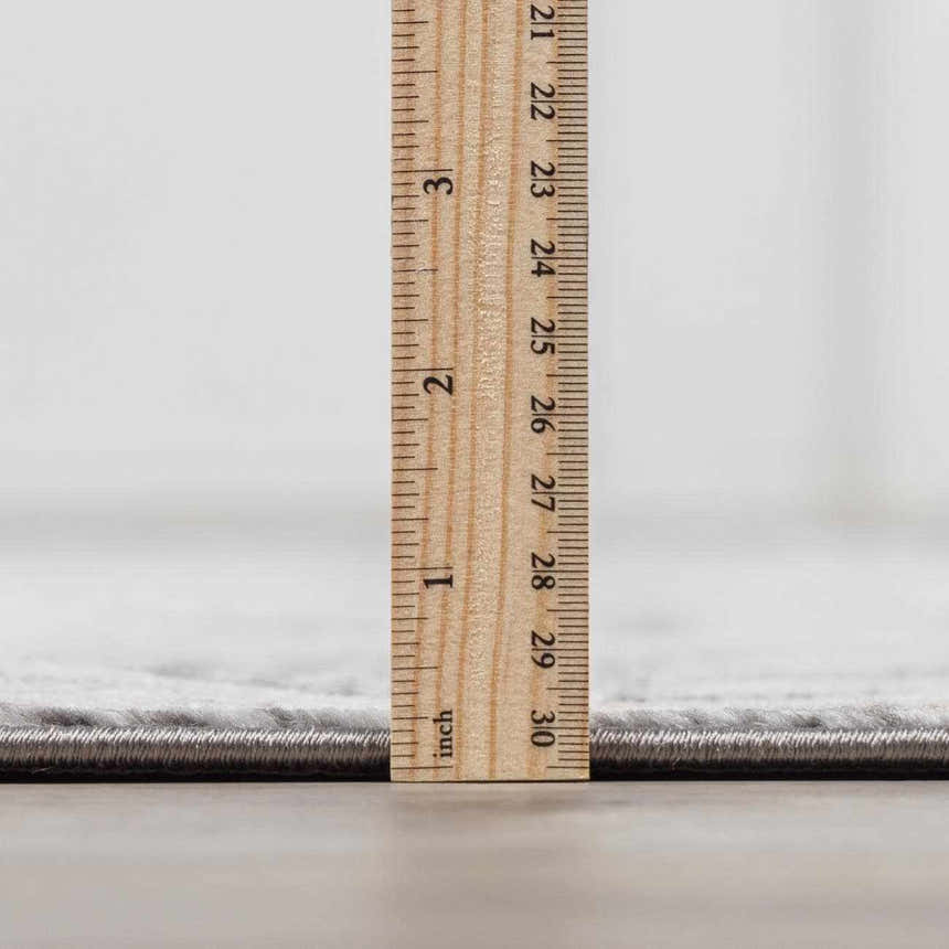 Close-up of the Minoa Area Rug's thickness, showing gray color and machine-woven construction. Pile