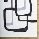 Close up of the Ulfah Area Rug. Hand tufted wool rug with a geometric design in ash and jet black. Corner