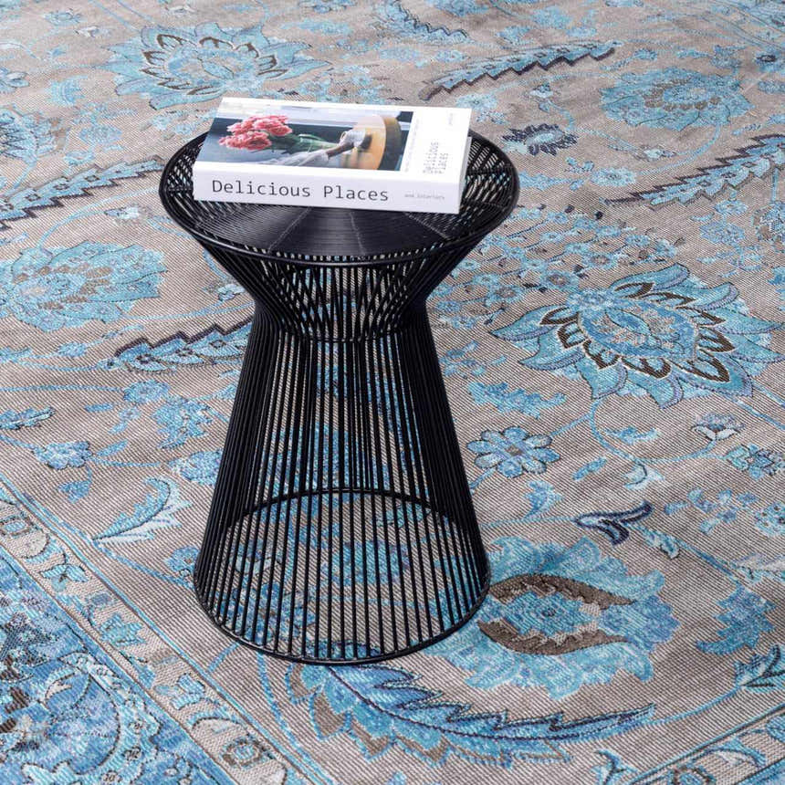 Close-up of the Mardina Turquoise Area Rug with beige and blue floral pattern, styled with a black accent table and book. Styleshot