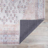 Close-up of the Moora Washable Area Rug showing its floral pattern, aqua, blush, and brown colors, and gray backing. Fold