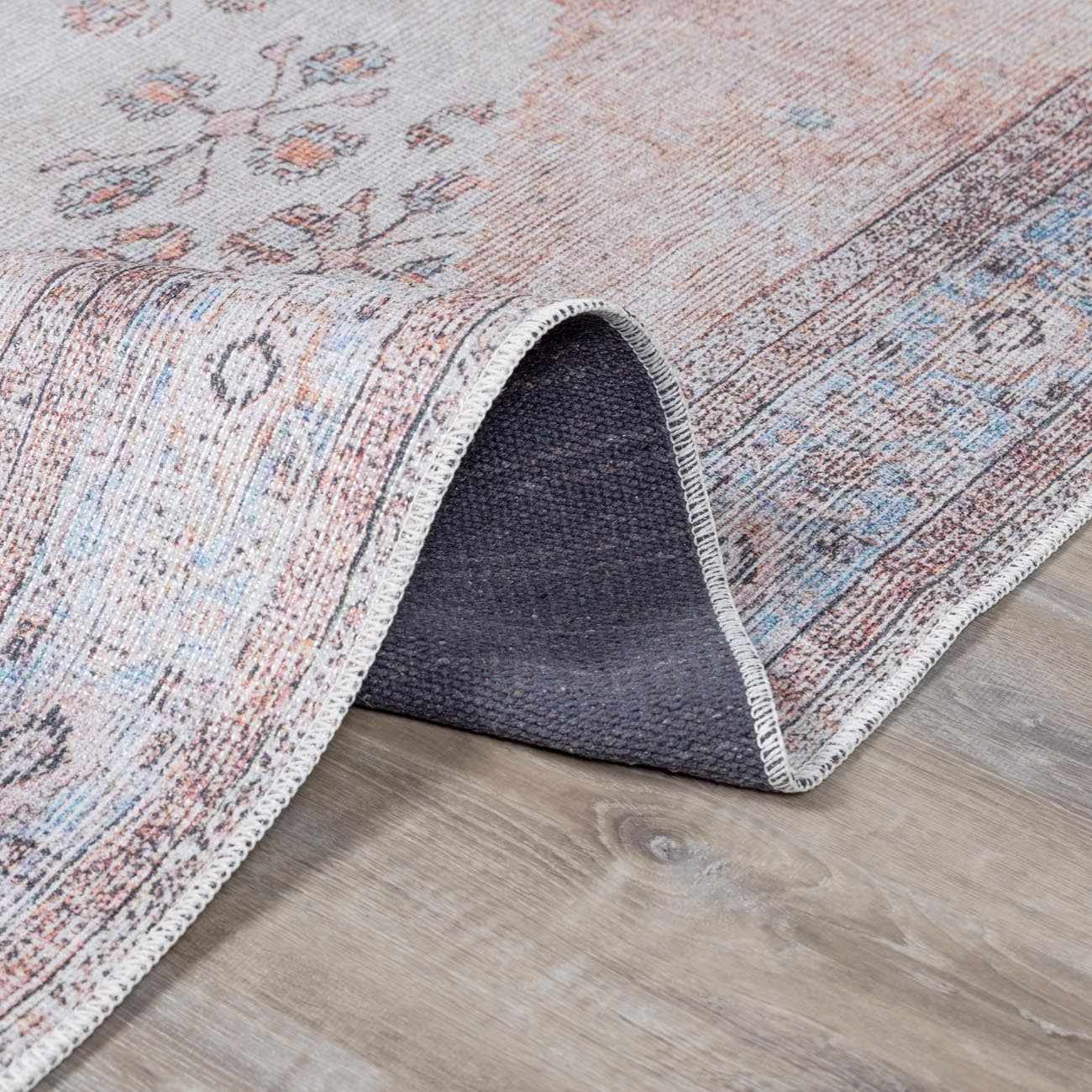 Close-up of the Moora Washable Area Rug showing its traditional floral pattern, aqua, blush, and gray colors, and soft chenille texture. Fold