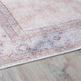 Close-up of the Moora Washable Area Rug. Features a traditional pattern in aqua, blush, brown, and coral hues. Chenille-Polyester texture. Corner