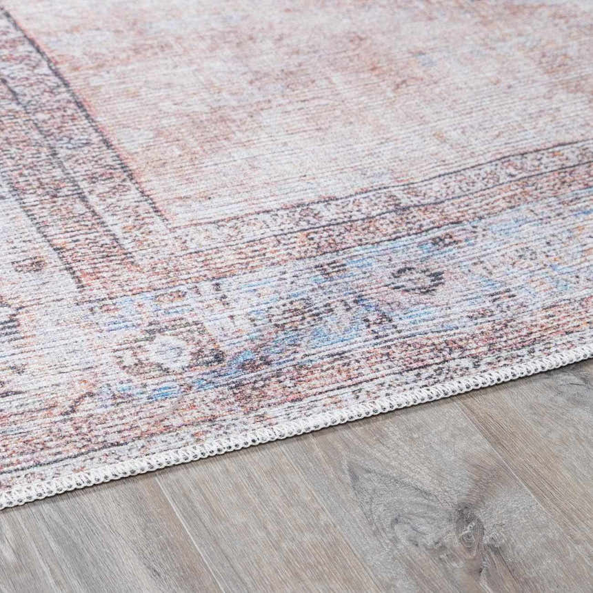Close-up of the Moora Washable Area Rug. Features a traditional pattern in aqua, blush, brown, and coral hues. Chenille-Polyester texture. Corner