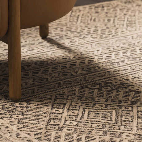 Close-up of the Nairne Textured Wool Area Rug with a black, gray, and taupe bohemian pattern under a chair. Roomscene-Rectangle