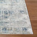Close-up of the Neron Thick Luxe Abstract Rug showing blue, cream, and charcoal abstract design on wood floor. Front
