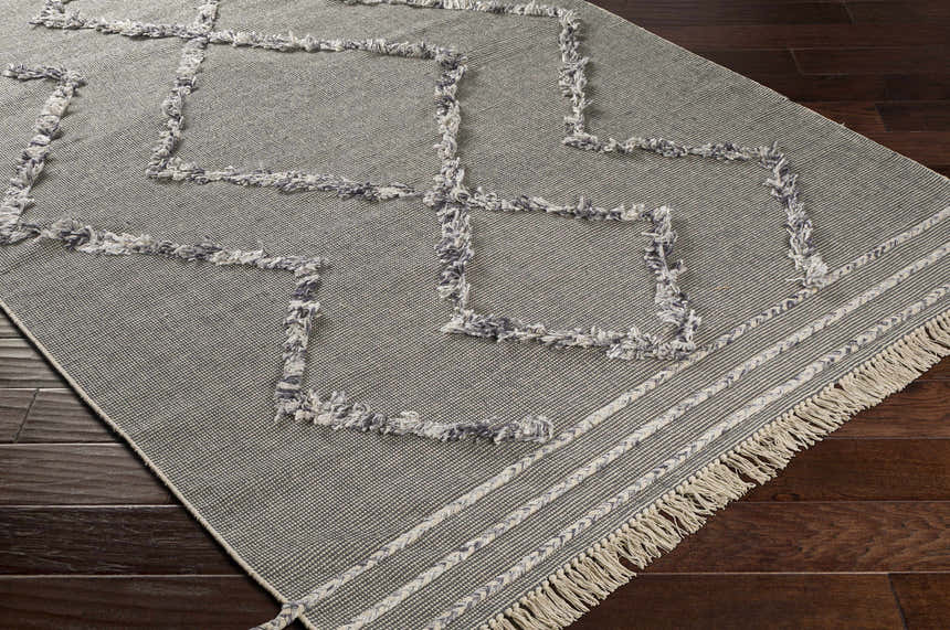 Close-up of the Needville Gray High-Low Rug, showcasing its geometric design, fringe detail, and hand-woven texture on a wood floor. Corner