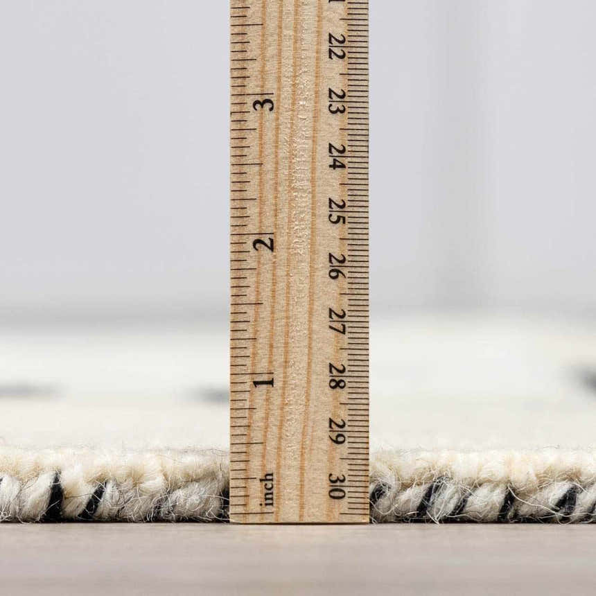 Close-up of the Brooklyn Modern Hand Tufted Wool Area Rug showing pile height with a ruler. Cream and black wool texture. Pile