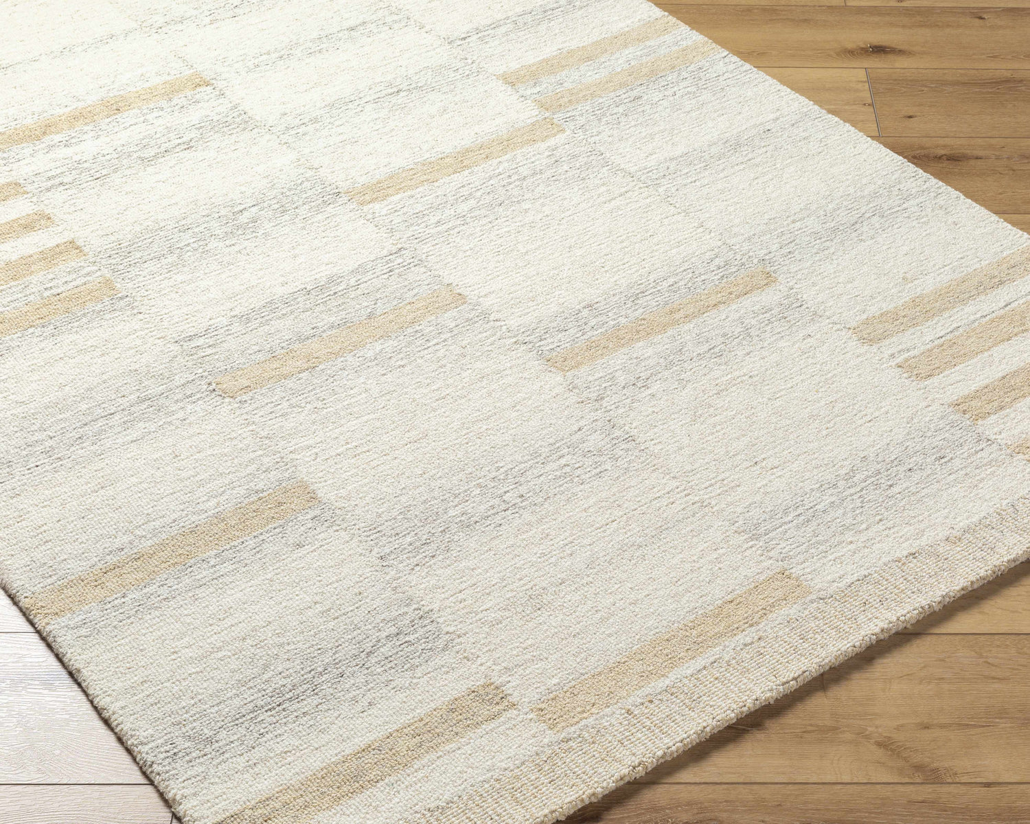 Close-up of the Max Handmade Becki Owens x LIVABLISS BOMX-2300 Area Rug. Cream wool rug with tan and taupe geometric stripes. Corner