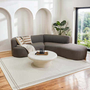 Living room scene with a Nimue Taupe Area Rug, gray sectional sofa, and white coffee table on wood floors. Roomscene-Rectangle
