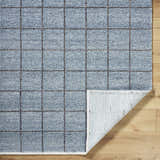 Close-up of the slate blue Ayinde Area Rug. Hand woven, recycled PET yarn rug with a contemporary grid pattern and textured pile. Fold
