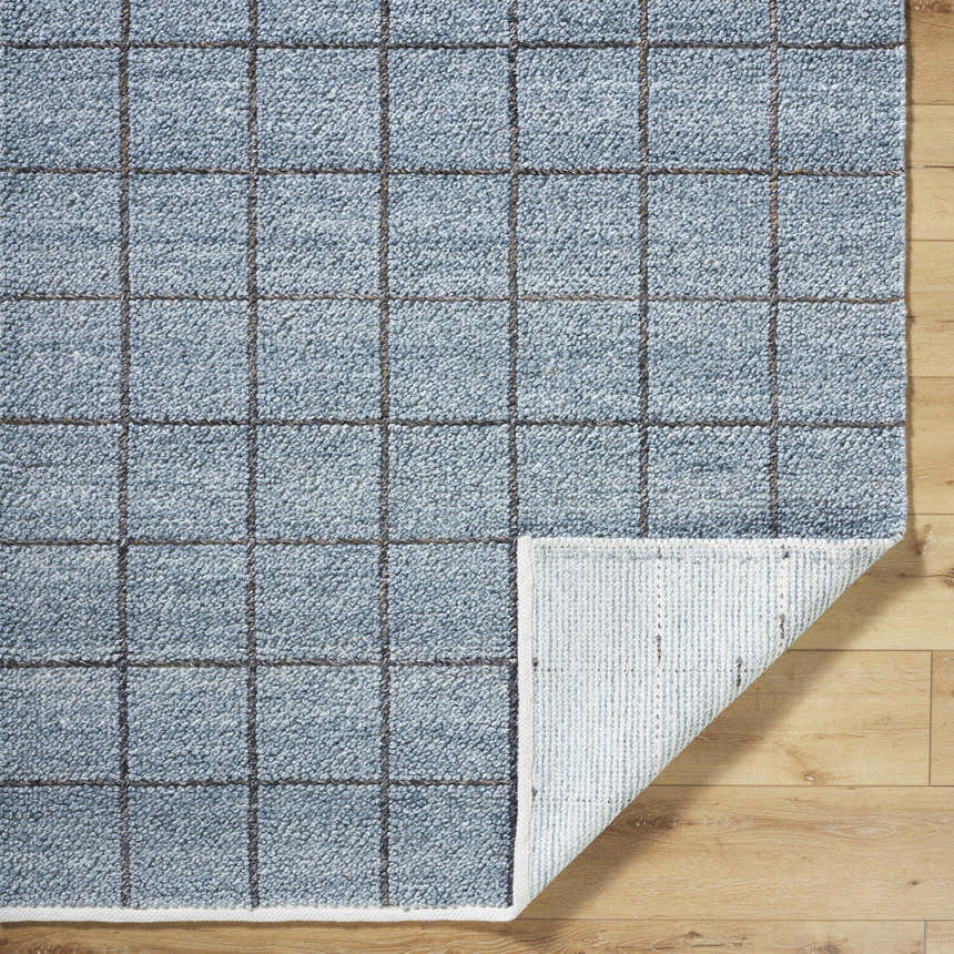 Close-up of the slate blue Ayinde Area Rug. Hand woven, recycled PET yarn rug with a contemporary grid pattern and textured pile. Fold
