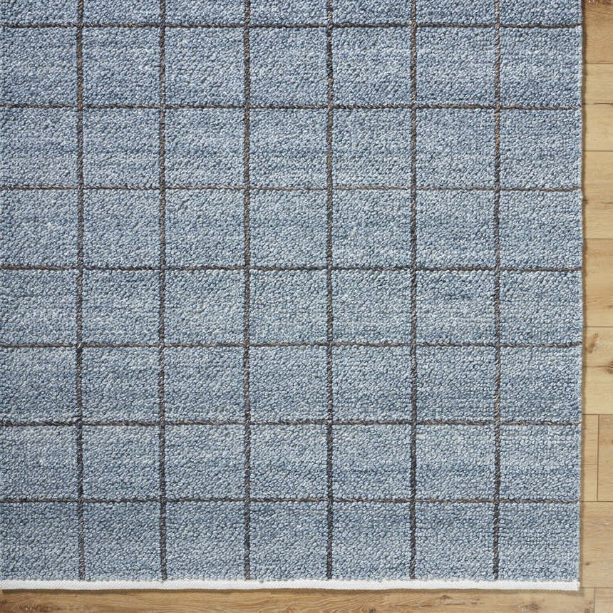 Close-up of the slate blue Ayinde Area Rug. Hand woven, recycled PET yarn rug with a contemporary grid pattern. Corner