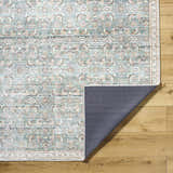 Close-up of the Ayanna Washable Area Rug. Machine-woven polyester rug in cream, teal, tan, and dark red with a traditional pattern. Fold