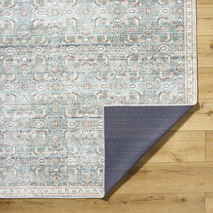 Close-up of the Ayanna Washable Area Rug. Machine-woven polyester rug in cream, teal, tan, and dark red with a traditional pattern. Fold