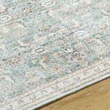 Close-up of the Ayanna Washable Area Rug. Traditional design in cream, teal, tan, and dark red on a wood floor. Texture