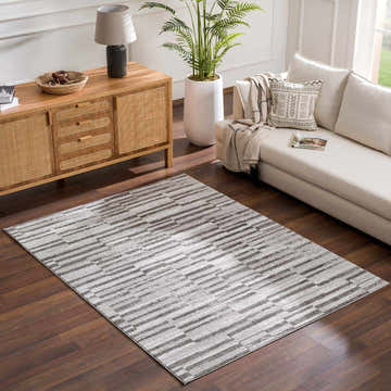 Living room scene with Arissa Broken-Striped Area Rug in black, gray, and white, styled with a sofa and wood cabinet. Roomscene-Rectangle