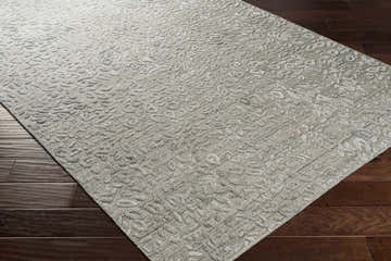 Close-up of the Newburn Area Carpet, a hand-loomed rug in charcoal, gray, and light gray with a subtle, textured pattern. Corner