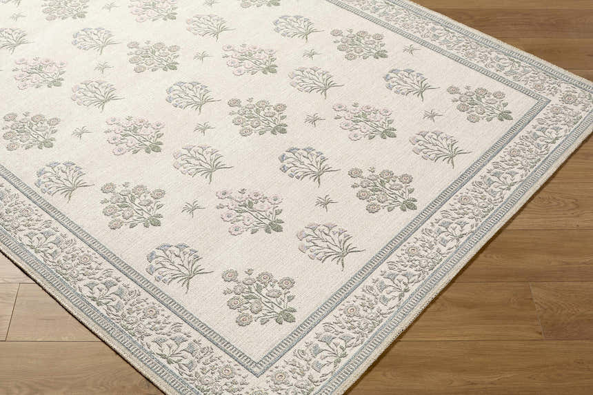 Close-up of the Aquene Ivory Washable Area Rug, featuring a floral pattern in blush, sage, and sky blue on an ivory background. Corner