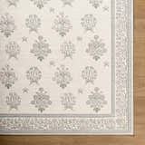 Close-up of Aquene Ivory Washable Area Rug. Features floral pattern in blush, sage, and sky blue with a decorative border. Corner
