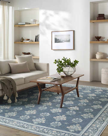 Living room scene with Aquene Denim Washable Area Rug, beige sofa, wood coffee table, and built-in shelves. Roomscene-Rectangle