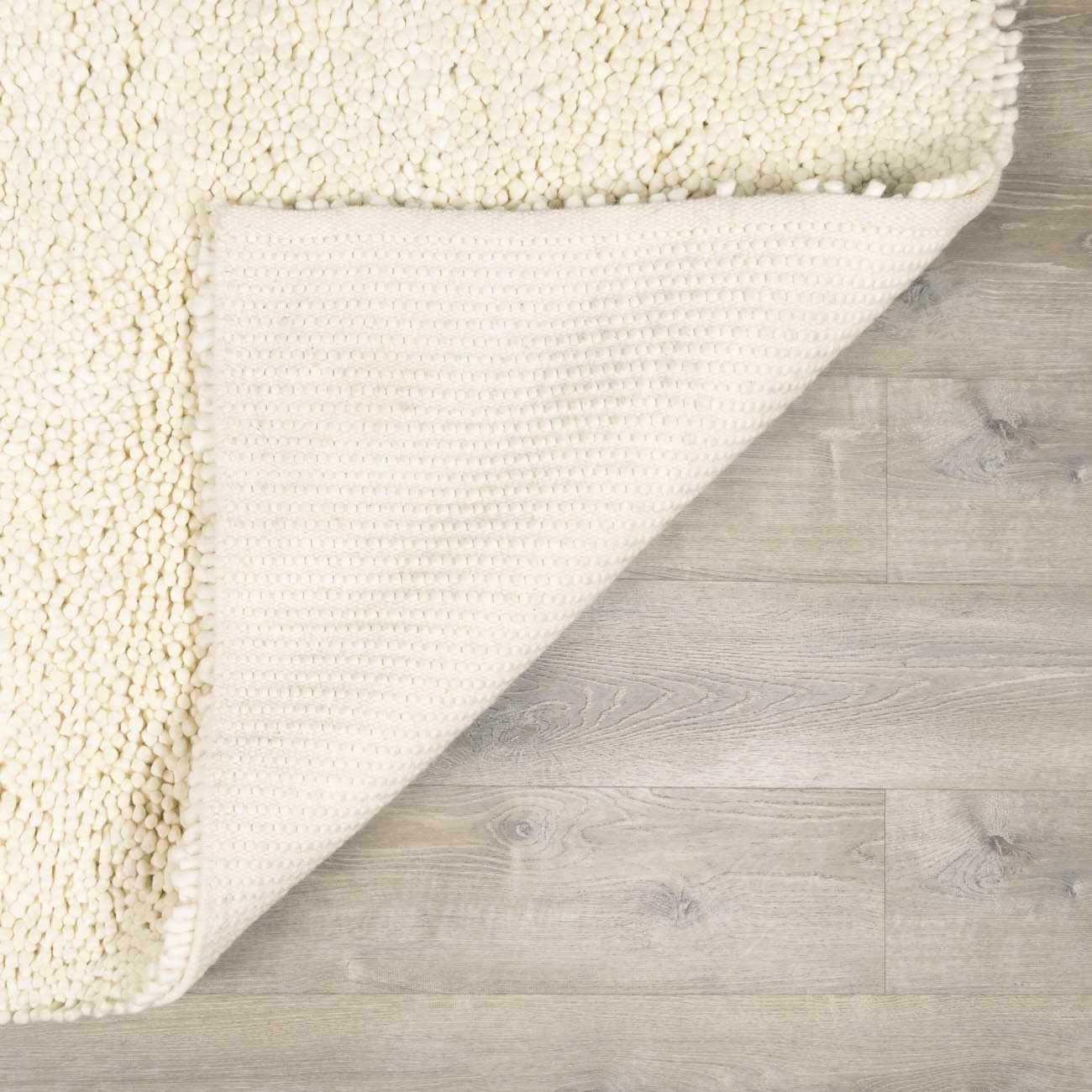 Close-up of the cream Oakridge Area Rug showing its looped wool texture and woven backing on wood floor. Fold