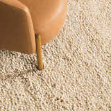 Close-up of the cream-colored, hand-woven Oakridge Area Rug showing its chunky, textured wool pile next to a leather chair. Styleshot