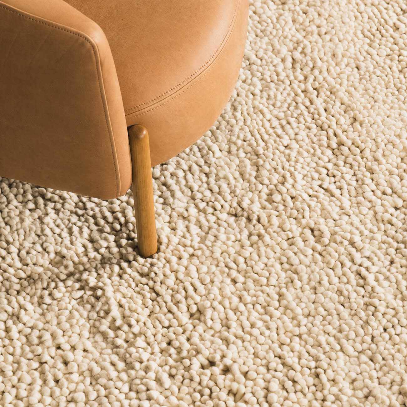 Close-up of the cream-colored, hand-woven Oakridge Area Rug showing its chunky, textured wool pile next to a leather chair. Styleshot