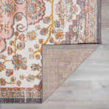 Close-up of the Oark Floral Medallion Area Rug. Features a floral pattern in brick red, camel, and dusty pink on an off-white base. Fold