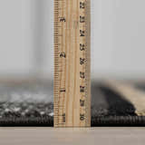 Close-up of the pile height of the Buckhaven Area Rug, showing black, gray and beige tones with a ruler. Pile