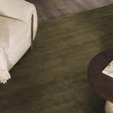 Close-up of a solid green Brockton wool rug in a living room with a cream chair and round wood coffee table. Styleshot