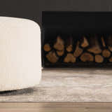 Close up of Pialba Thick Luxe Abstract Smokey Rug in a living room with a fireplace and white ottoman. Swatch