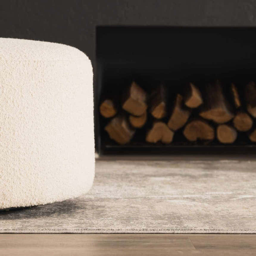 Close up of Pialba Thick Luxe Abstract Smokey Rug in a living room with a fireplace and white ottoman. Swatch