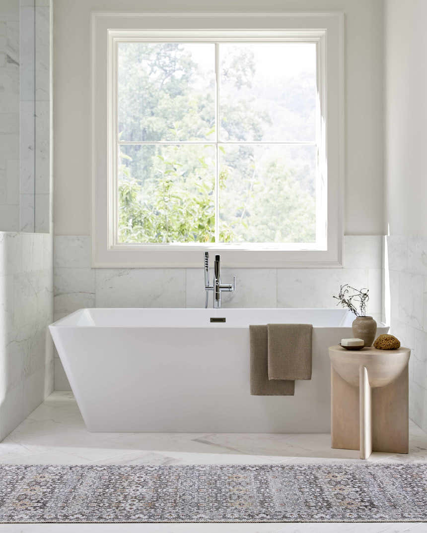 Bright bathroom scene with a white tub and Our PNW Home Rainier Damask Brown Washable Rug on the marble floor. Roomscene-Rectangle