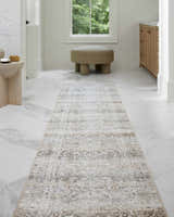 Light brown Rainier Damask Washable Rug runner in a bright bathroom with marble floors, tan stool, and wood vanity. Roomscene-Runner