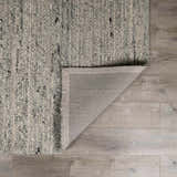 Close-up of the hand-woven Olisa Gray Wool Area Rug showing texture and backing on light wood floors. Fold