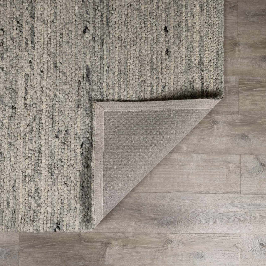 Close-up of the hand-woven Olisa Gray Wool Area Rug showing texture and backing on light wood floors. Fold