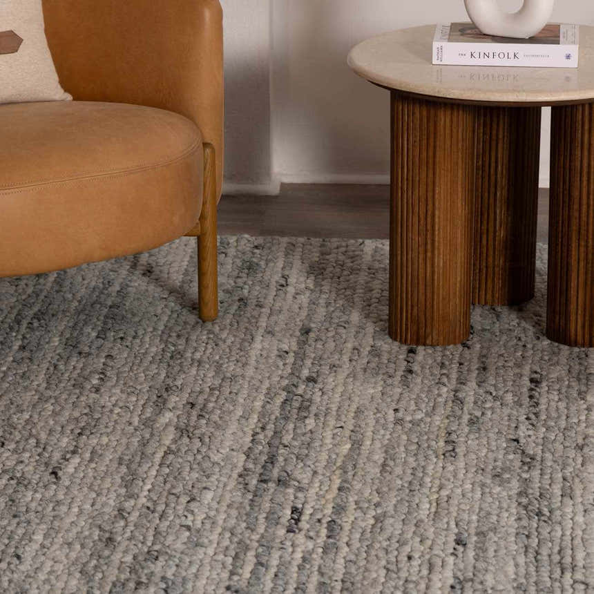 Close up of the Olisa Gray Wool Area Rug showing its texture next to a leather chair and wood side table. Roomscene-Rectangle