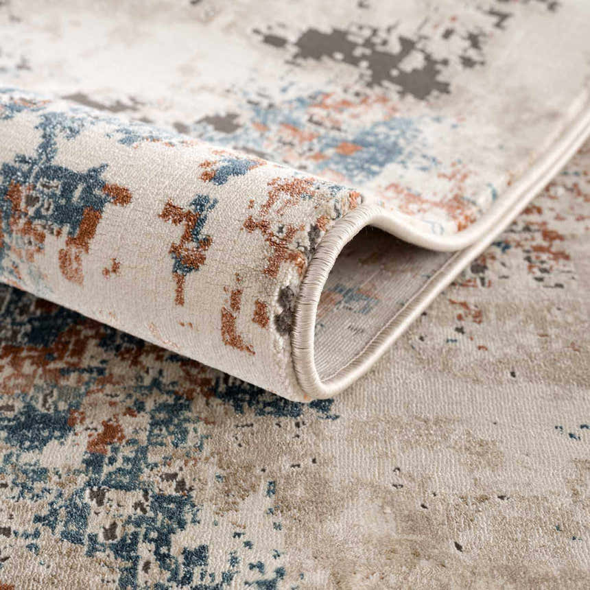 Close-up of the Priscilla Area Rug showing its abstract pattern, burnt orange, blue, and beige colors, and soft texture. Fold
