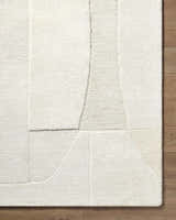 Close-up of the Agneza Area Rug, a hand-tufted wool rug with a geometric design in beige, cream, ivory, and tan. Corner