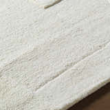 Close-up of the hand-tufted Agneza Area Rug showing its plush, ivory wool texture and subtle geometric pattern. Texture