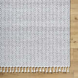 Close-up of the Anelia Medium Gray Area Rug featuring a diamond pattern and fringe on a wood floor. Corner