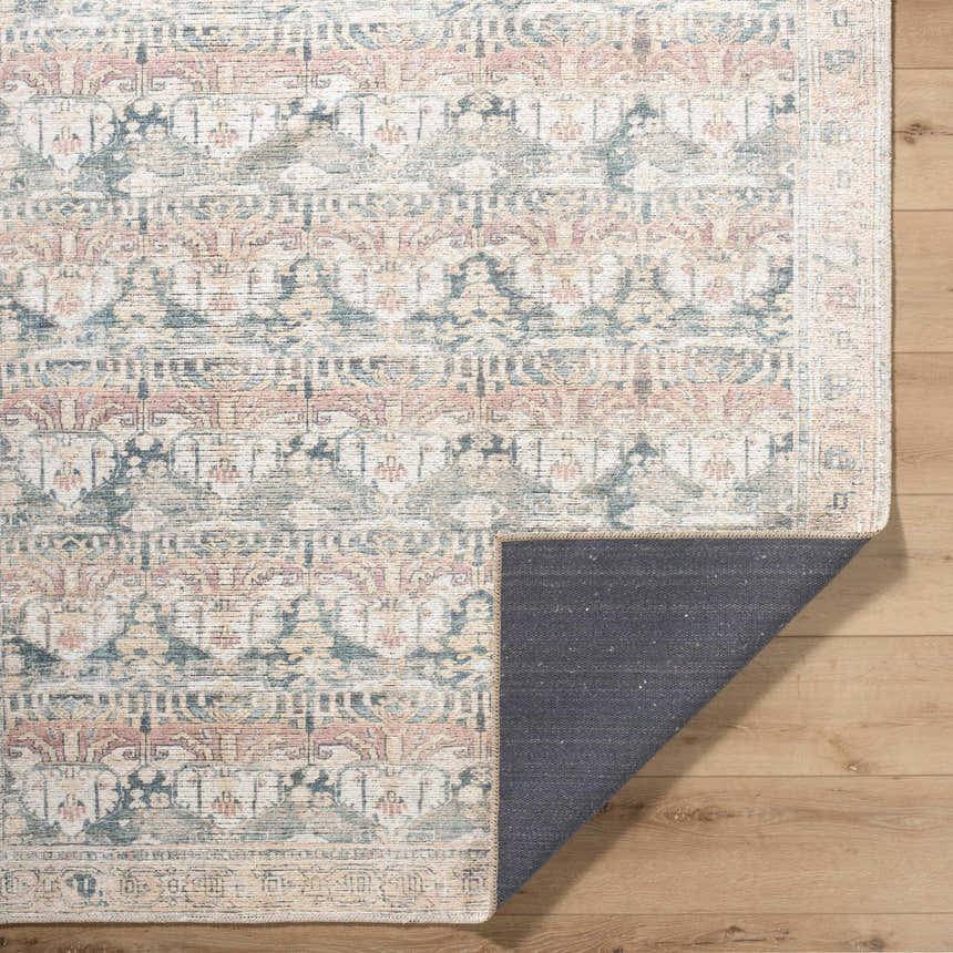 Close-up of the Arushi Washable Area Rug. Cream rug with traditional design in green, orange, and rust on wood floor. Fold