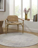 Sunlit room with a woven chair on a round Razi Avant Garde rug in gray, brown, and sage. Books and flowers on the window sill. Roomscene-Round