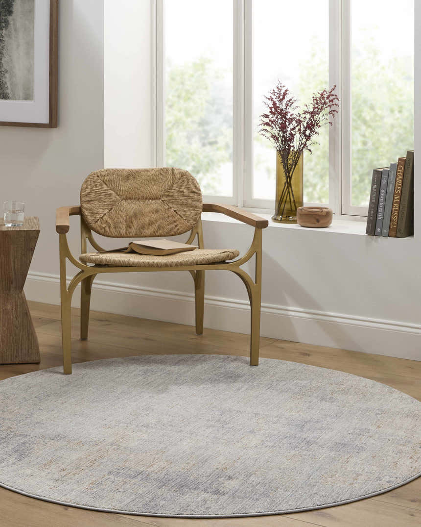 Sunlit room with a woven chair on a round Razi Avant Garde rug in gray, brown, and sage. Books and flowers on the window sill. Roomscene-Round