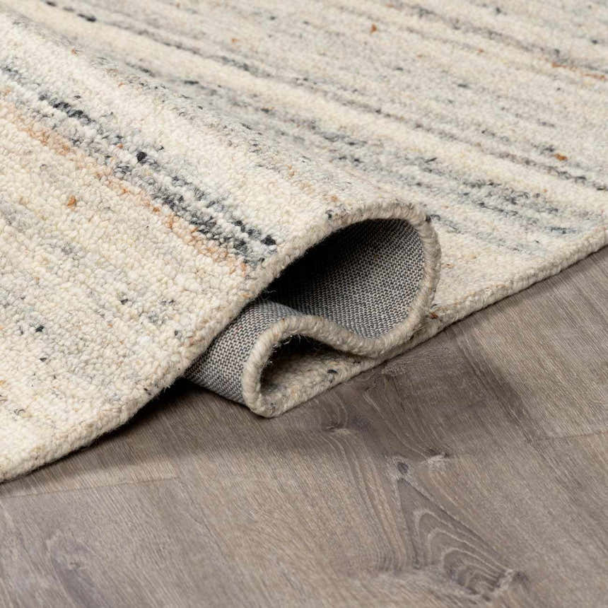 Close-up of the hand-tufted Capote Ivory Area Rug showing wool texture and charcoal, tan, and taupe color variations. Fold