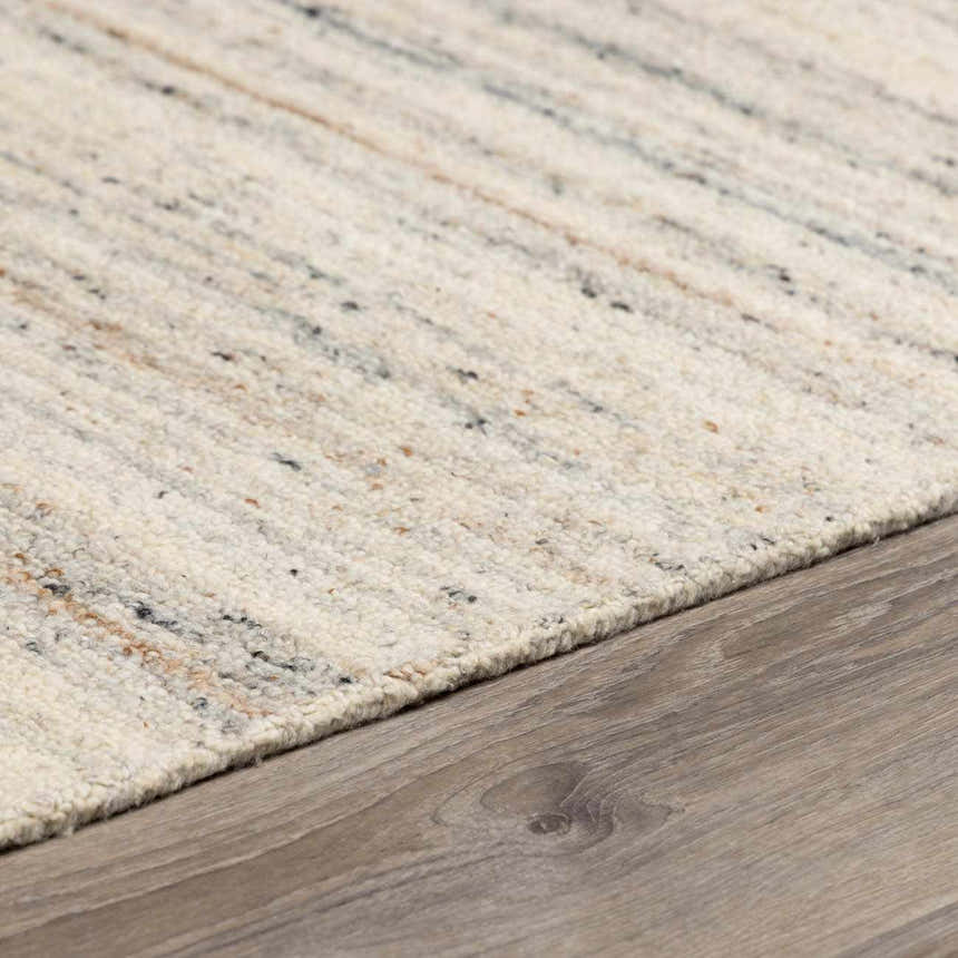 Close-up of the hand-tufted Capote Ivory Area Rug showing wool texture and charcoal, tan, and taupe color variations. Pile