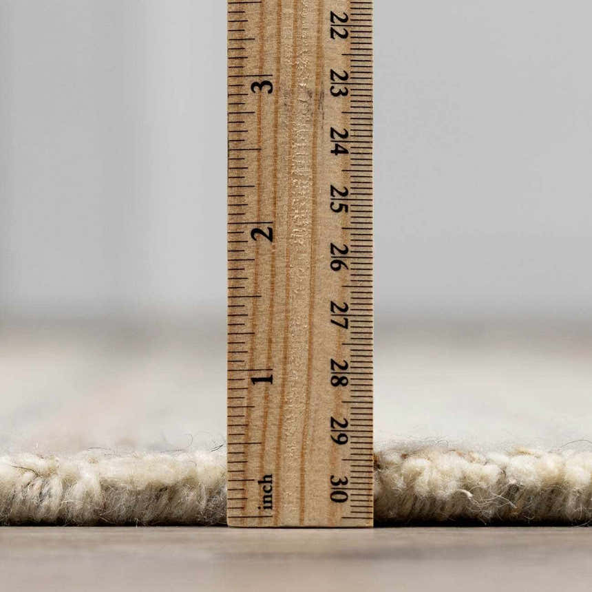 Close-up of the Capote Ivory Area Rug showing its pile height of approximately 1 inch with a ruler. Pile