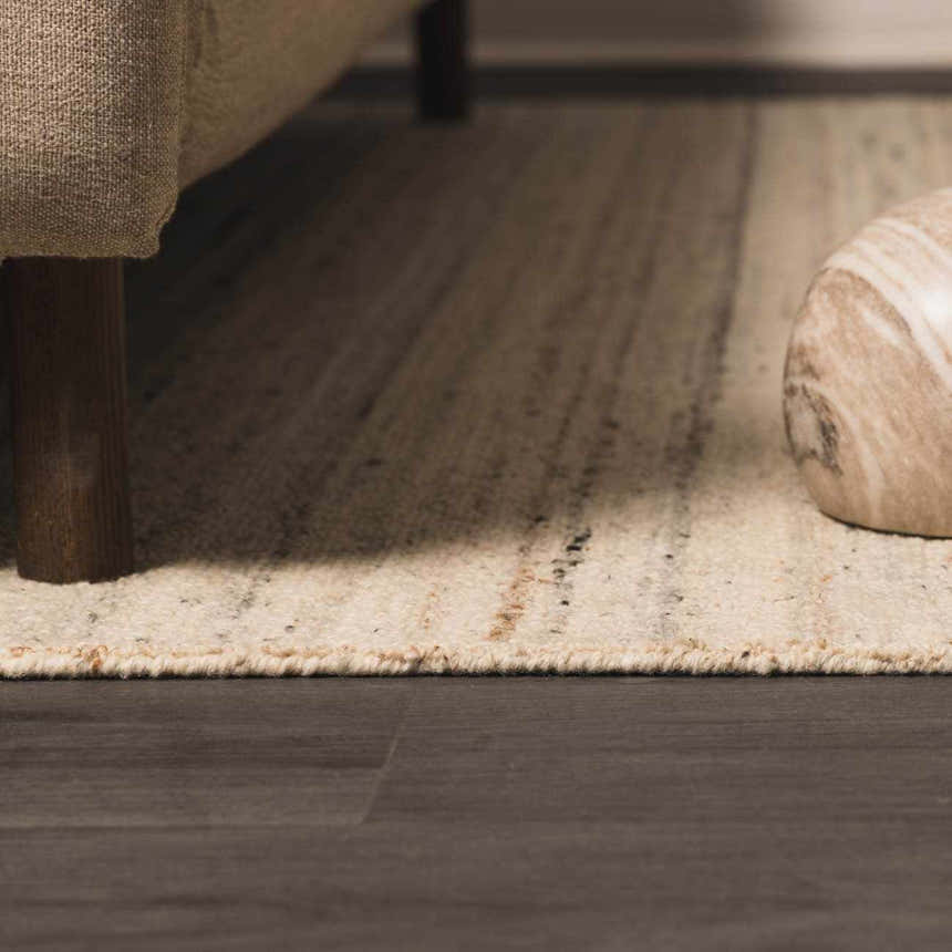 Close-up of the hand-tufted Capote Ivory Area Rug showing its ivory, charcoal, and tan tones and textured wool construction. Roomscene-Rectangle
