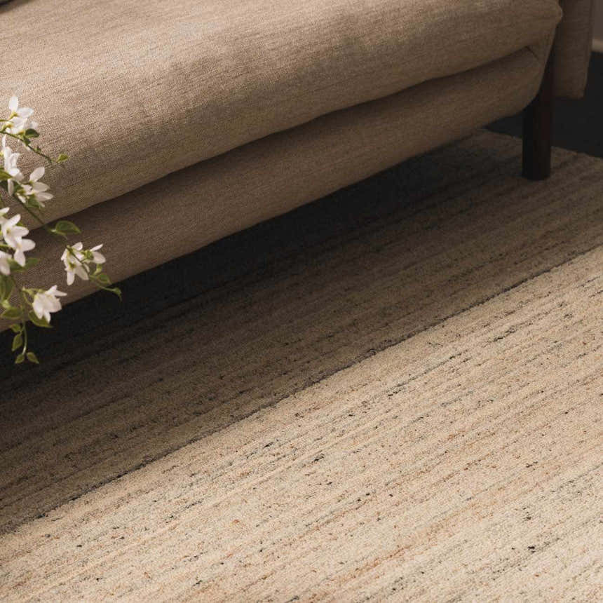 Close-up of the Capote Ivory Area Rug showing its textured wool design, ivory and charcoal colors, and subtle linear pattern. Roomscene-Rectangle
