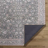 Close-up of the Anando Washable Area Rug showing a traditional floral pattern in cream, green, orange, and pale pink. Fold